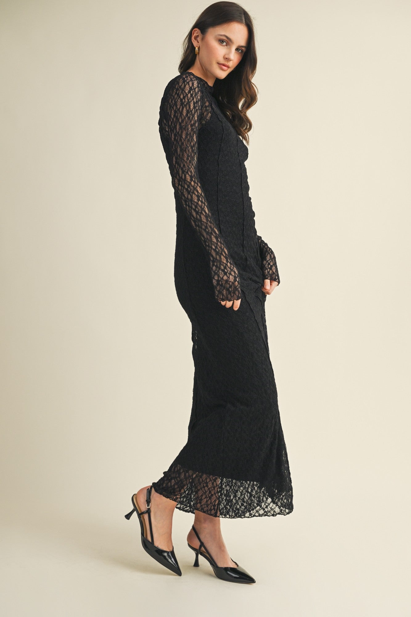 woman wearing a black lace long sleeve maxi dress with fitted silhouette and side slit, paired with black pointed toe heels