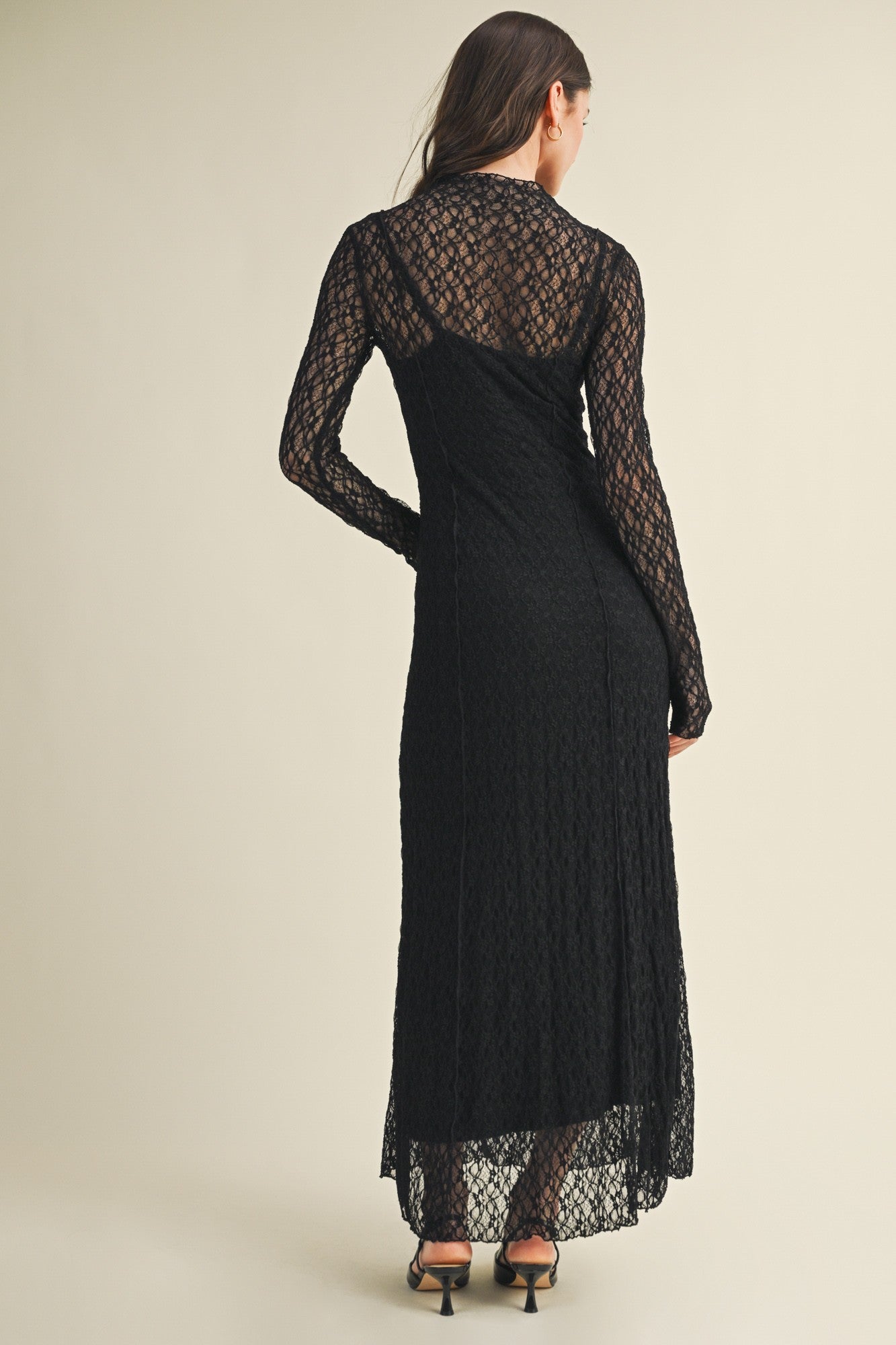woman wearing a black lace long sleeve maxi dress with a fitted silhouette and open back detailing