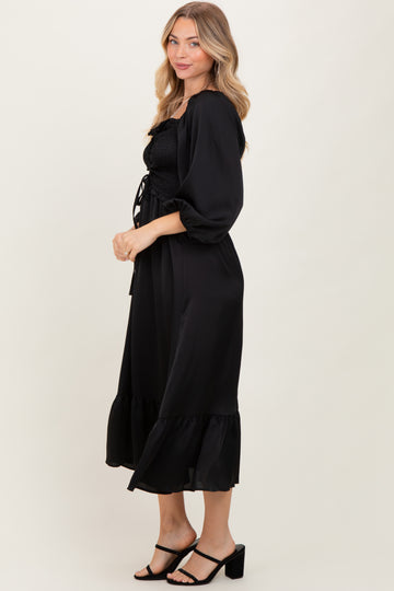 woman wearing a black smocked maxi dress with puff sleeves and a ruffled hem, posed sideways against a neutral background