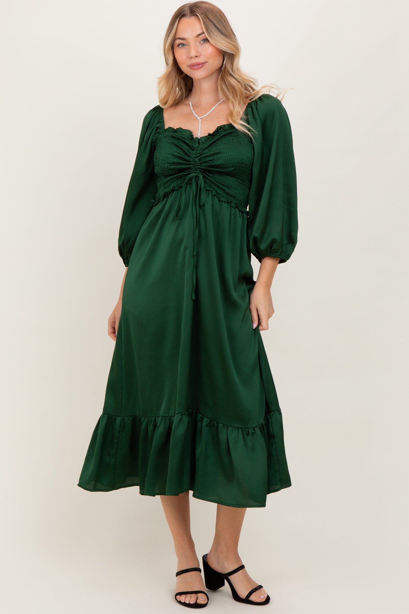 woman wearing a dark green puff sleeve midi dress with a gathered front and ruffle hem, standing in a relaxed pose