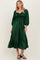 woman wearing a dark green puff sleeve midi dress with a gathered front and ruffle hem, standing in a relaxed pose