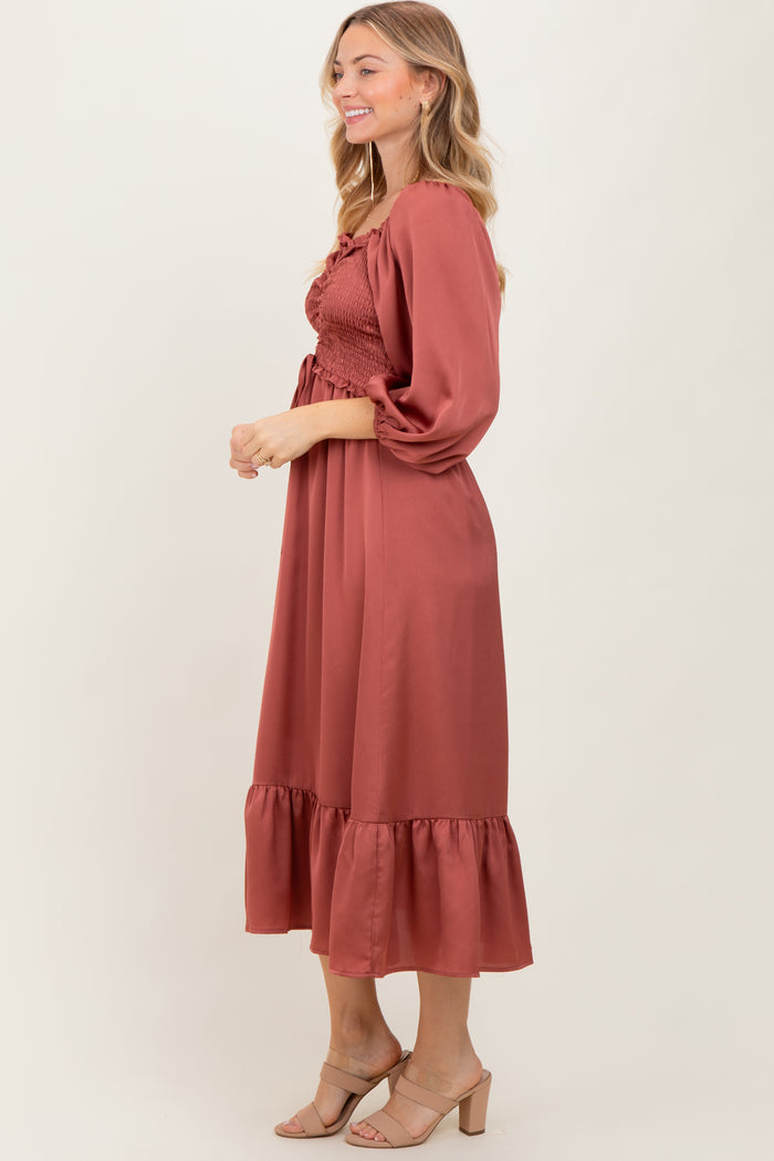 woman wearing a rust-colored midi dress with smocked bodice and puff sleeves, styled with nude heels