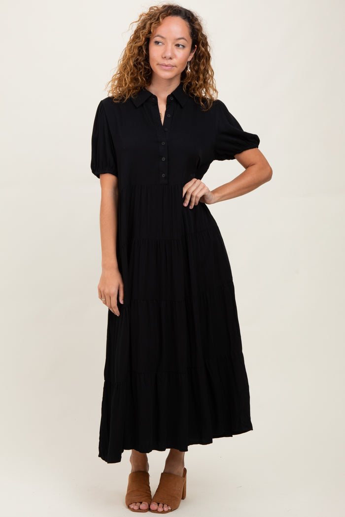 woman wearing a black tiered maxi dress with short puff sleeves and button-down front, standing on a neutral background