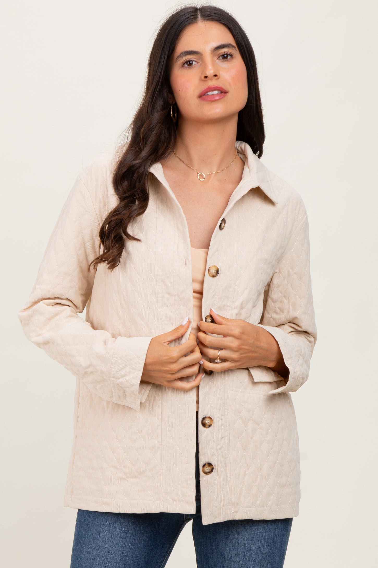 woman wearing a beige quilted jacket with a button front and long sleeves, styled with a neutral top and denim jeans