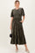 woman wearing a dark green smocked velvet maxi dress with short puff sleeves and a tiered skirt, holding a small handbag
