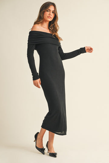 woman wearing a black off-the-shoulder long sleeve dress, styled with a fitted silhouette and high slit, paired with black heels