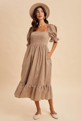 woman wearing a taupe puff sleeve midi dress with a square neckline and ruffled hem, styled with a hat and flats