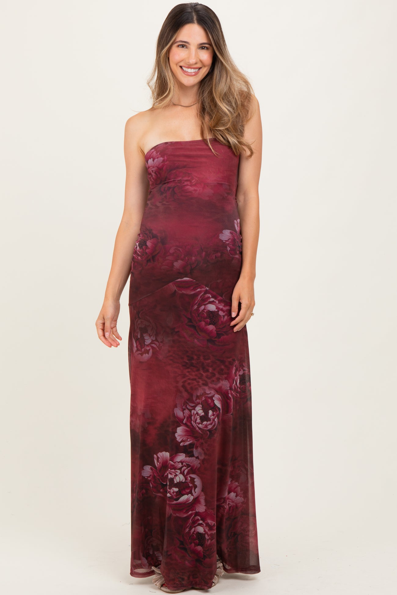 woman wearing a burgundy strapless maternity maxi dress with a floral pattern and a visible baby bump