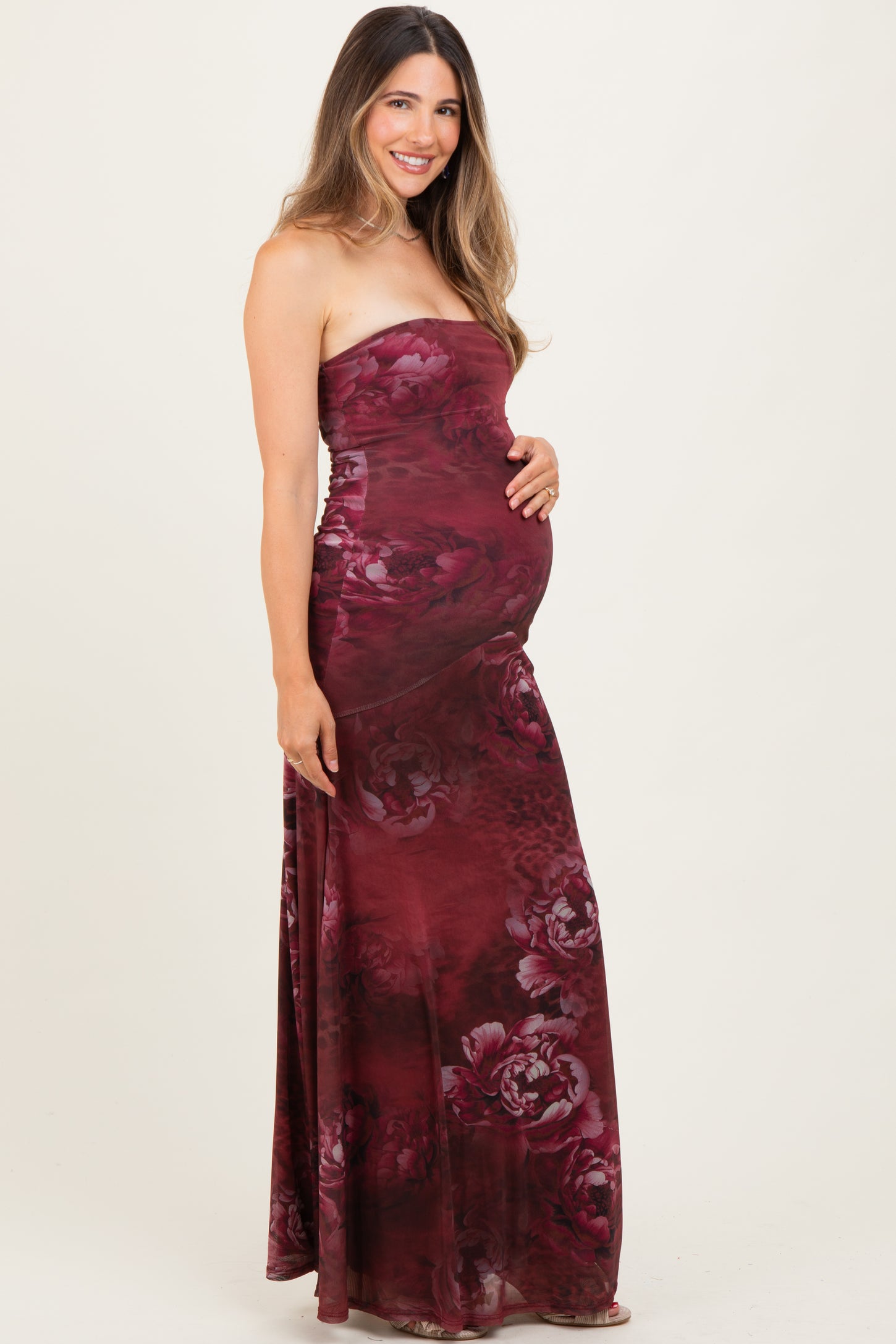 woman wearing a burgundy floral strapless maternity maxi dress and holding her baby bump