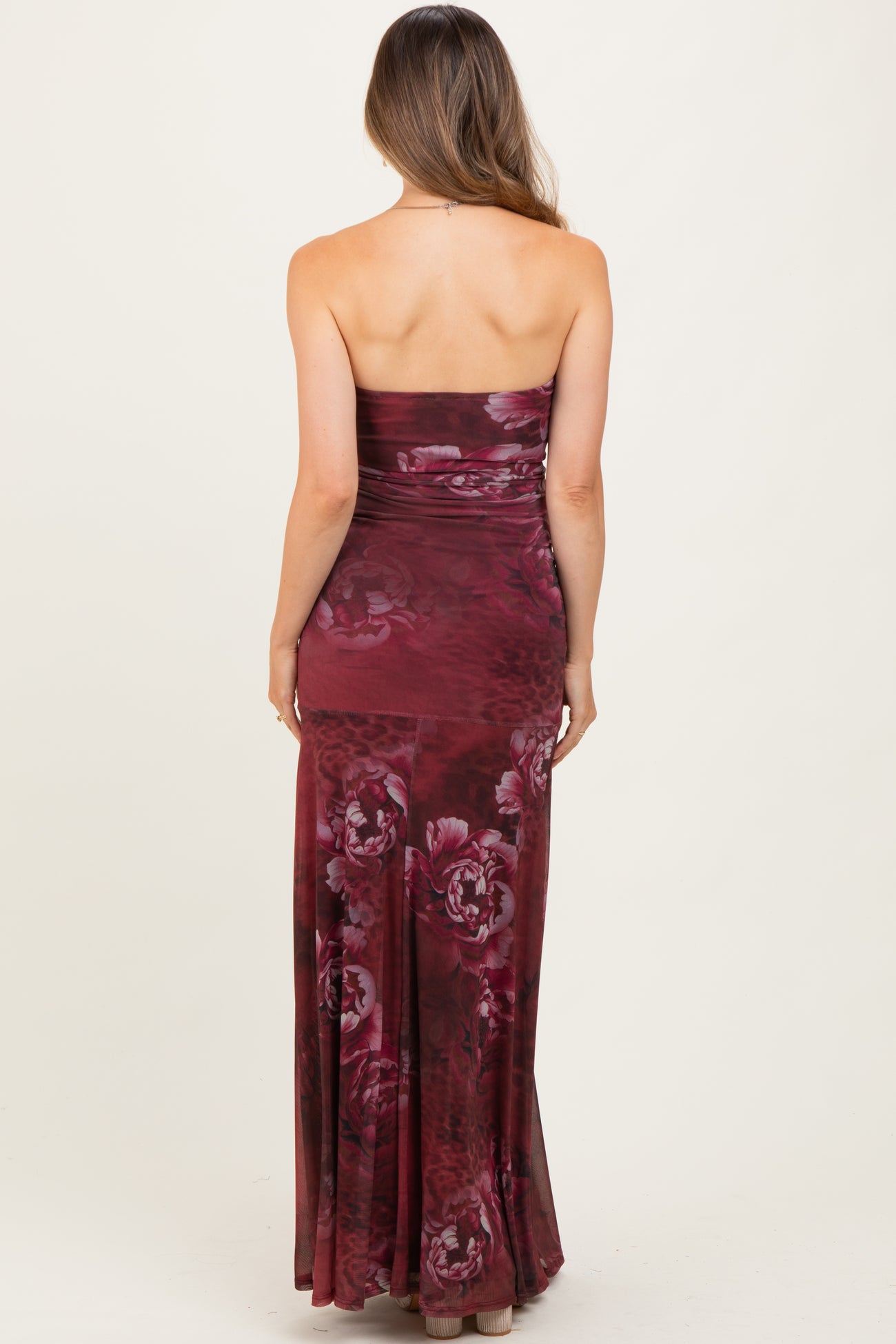 woman wearing a burgundy floral strapless maternity dress with a fitted silhouette and a long flowy skirt