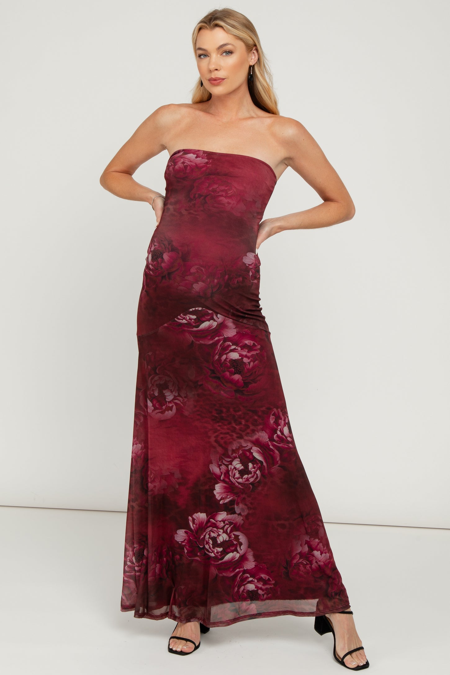woman wearing a burgundy strapless maternity maxi dress with floral design and a visible baby bump