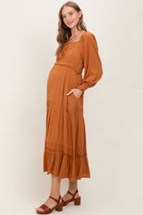 woman wearing a rust colored maternity maxi dress with puff sleeves and a tiered skirt, showing her baby bump