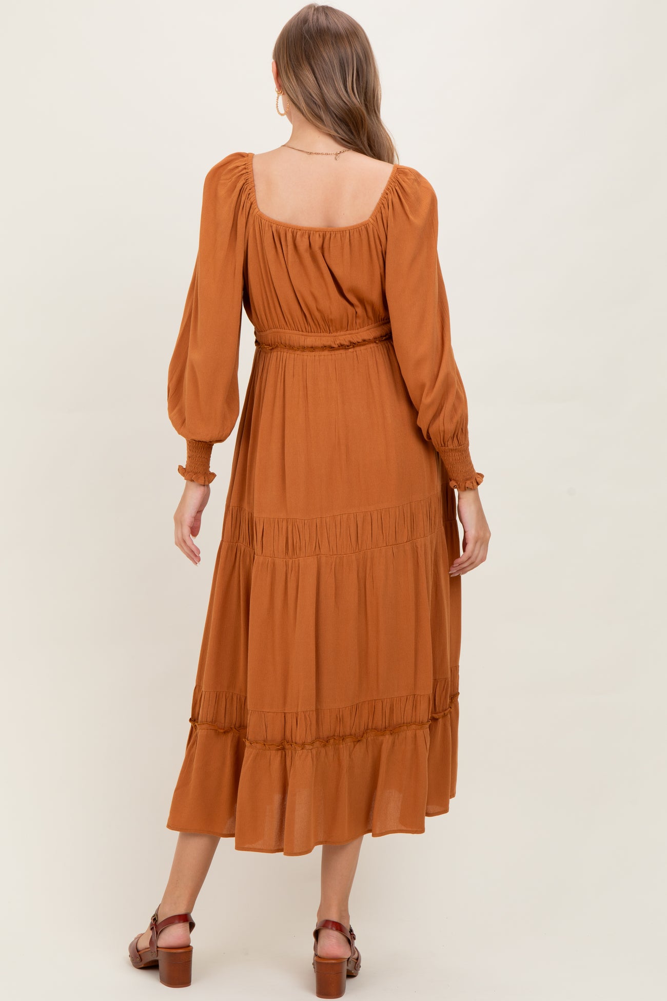 woman wearing a rust-colored maternity maxi dress with puffed sleeves and ruffle detailing