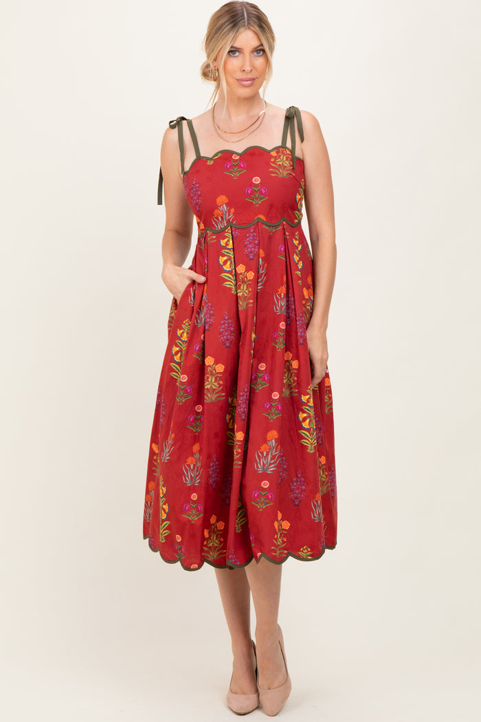woman wearing a red floral midi dress with scalloped details and tie straps, styled with pockets and nude heels