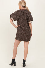 woman wearing a brown leopard print short dress with puff sleeves and stripe details, standing with her back to the camera