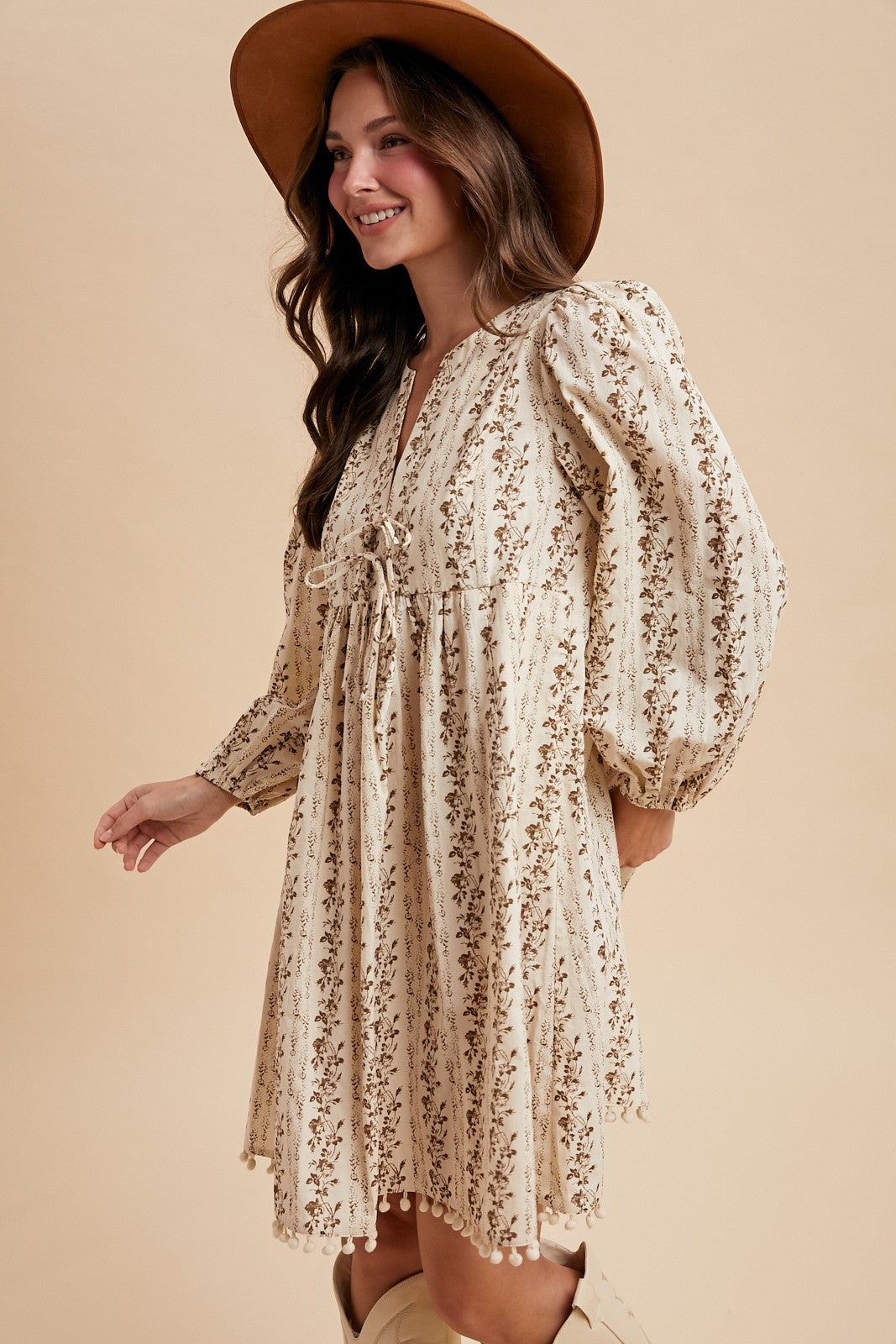 woman wearing a cream floral print puff sleeve dress with a drawstring waist and a wide-brimmed hat