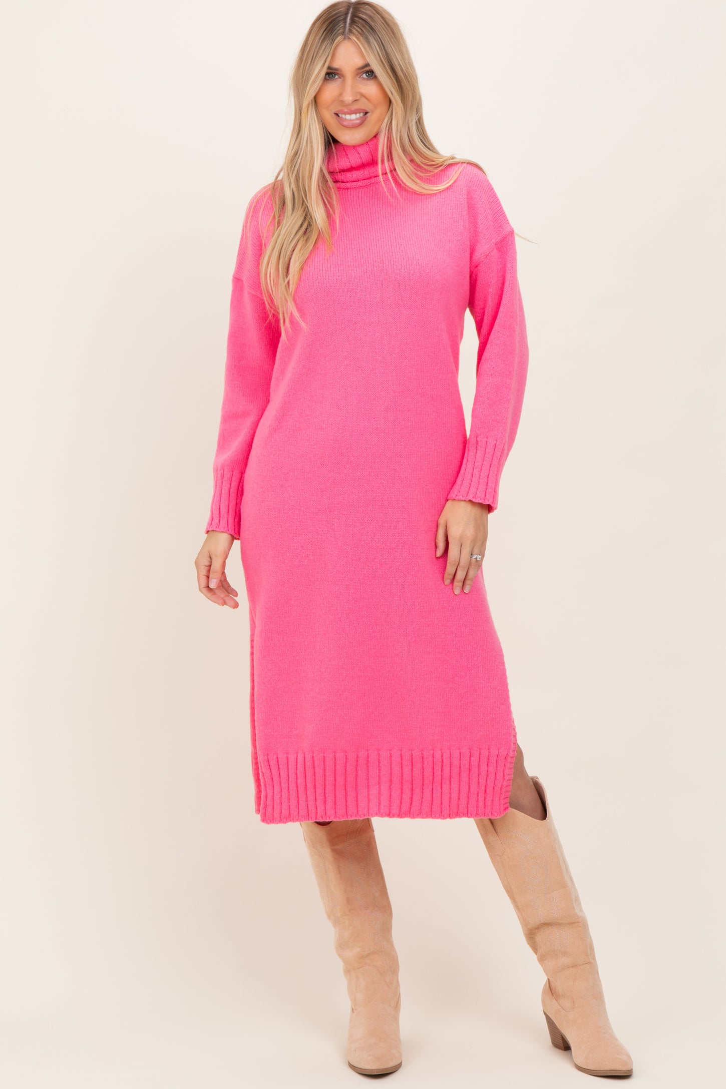 woman wearing a bright pink knitted turtleneck dress with ribbed details and tan knee-high boots