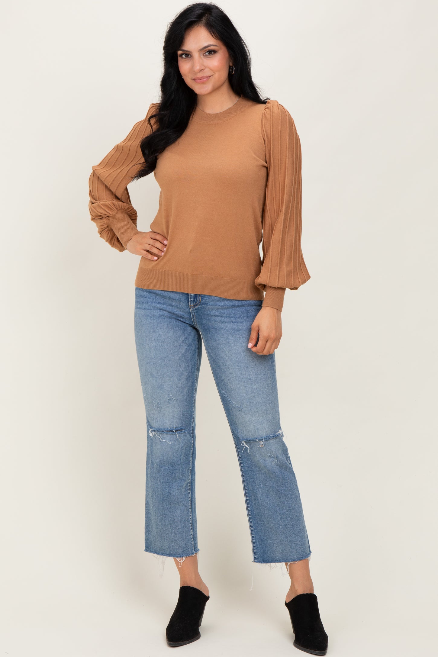 woman wearing a light brown sweater with pleated balloon sleeves and blue cropped jeans