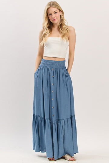 woman wearing a light blue maxi skirt with a tiered hem and buttons, paired with a white cropped top