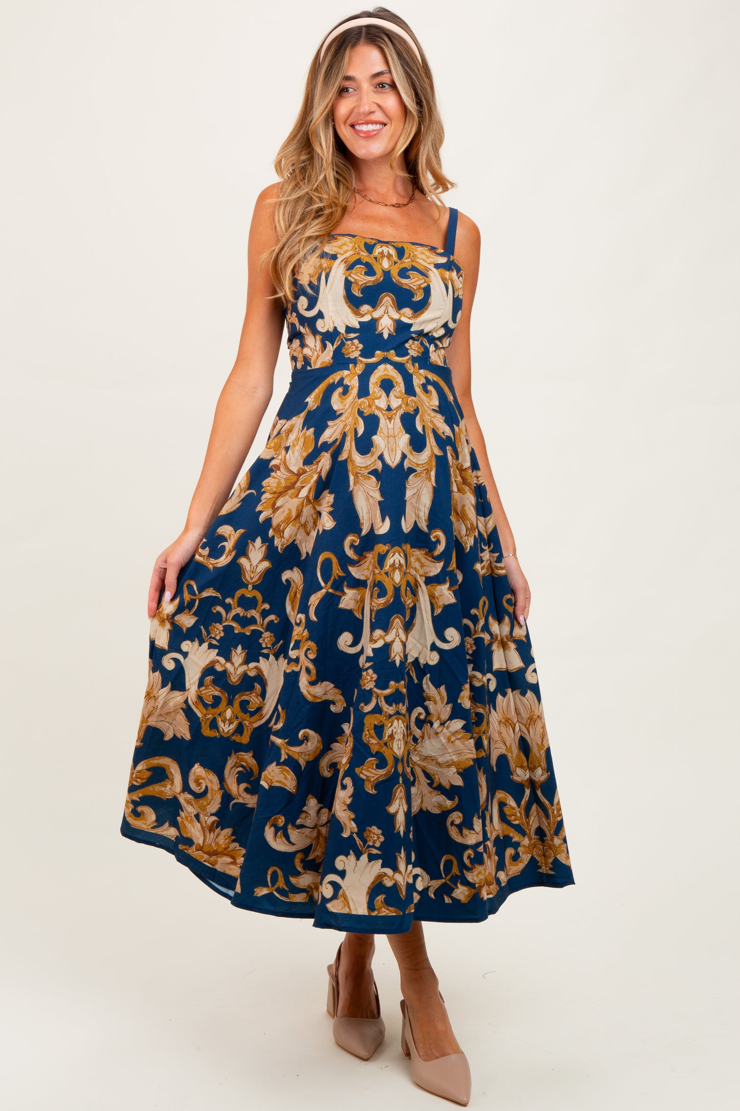 woman wearing a navy blue maternity dress with floral gold patterns and thin straps, showing her baby bump