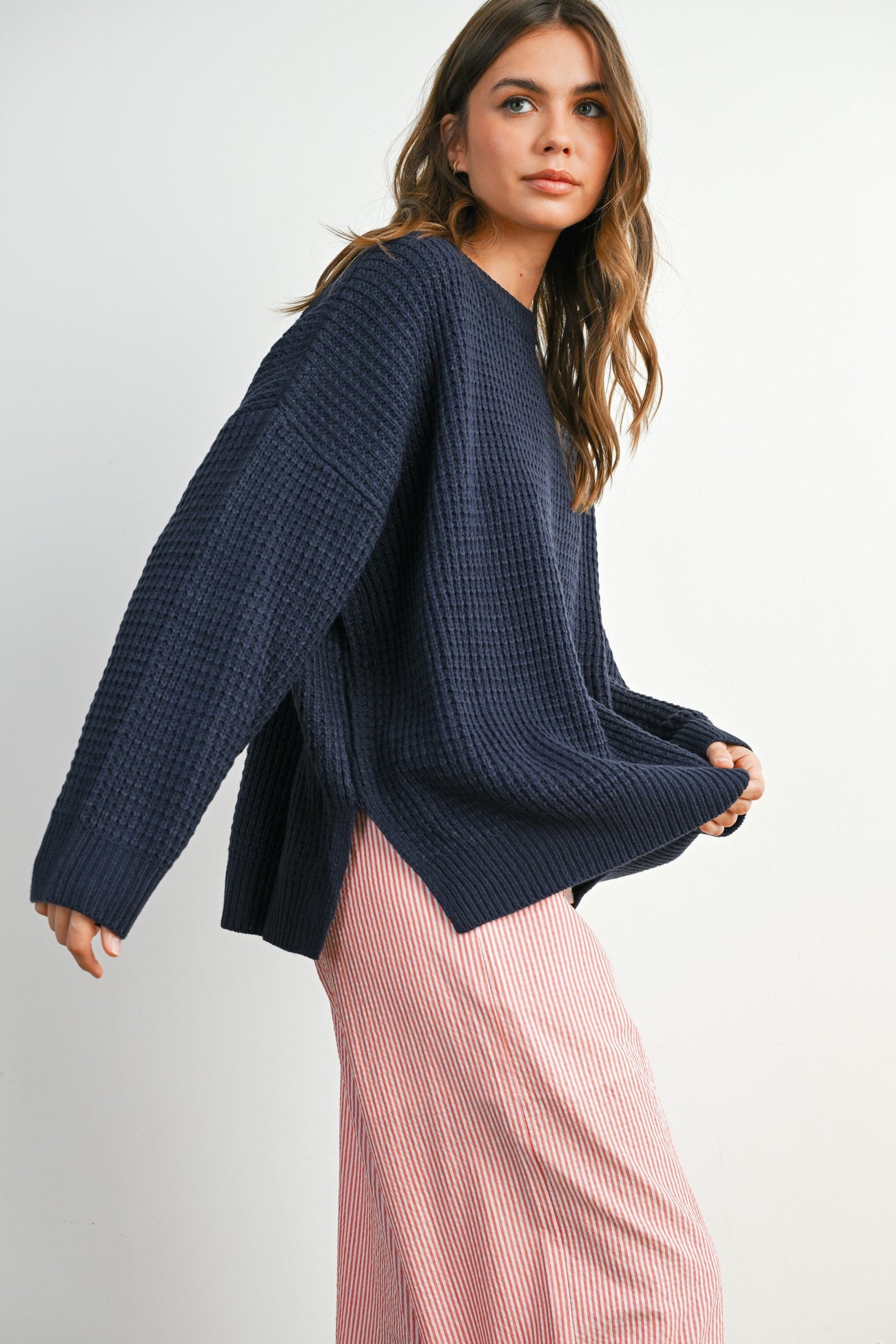 woman wearing a navy oversized waffle knit sweater and a striped pink maxi skirt