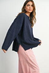 woman wearing a navy oversized waffle knit sweater and a striped pink maxi skirt