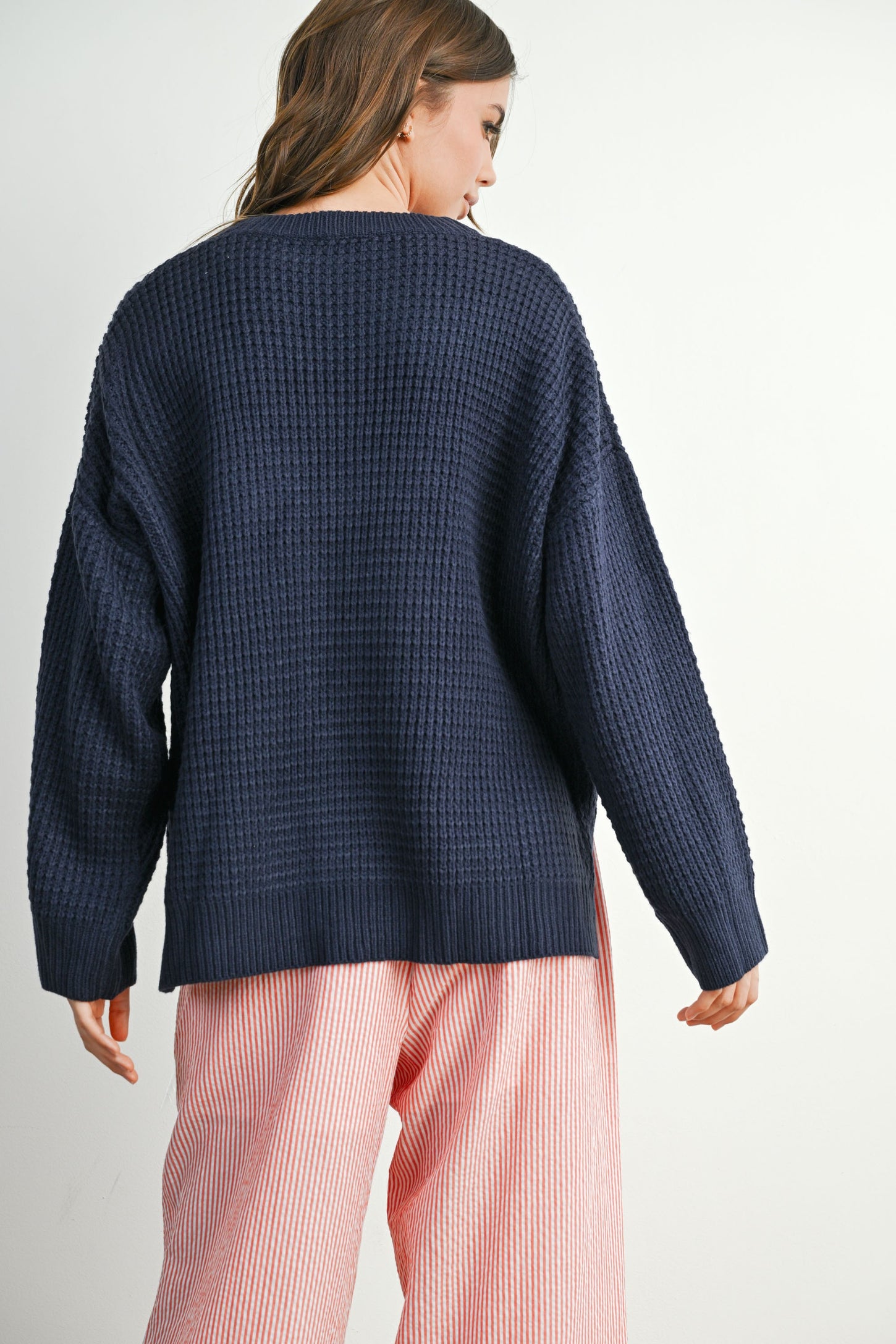 woman wearing a navy blue oversized textured sweater and pink striped wide-leg pants, viewed from the back