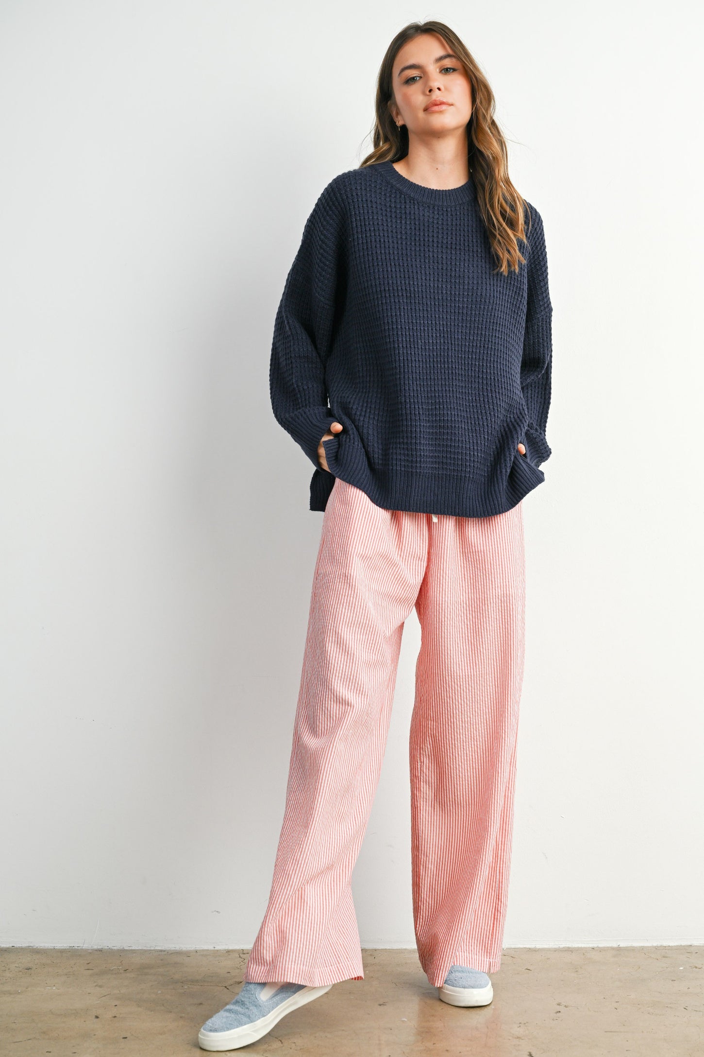 woman wearing a navy blue oversized waffle knit sweater and pink striped wide-leg pants