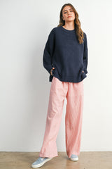 woman wearing a navy blue oversized waffle knit sweater and pink striped wide-leg pants