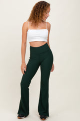 woman wearing a white cropped tank top and green flared pants, standing sideways with one hand on her hip