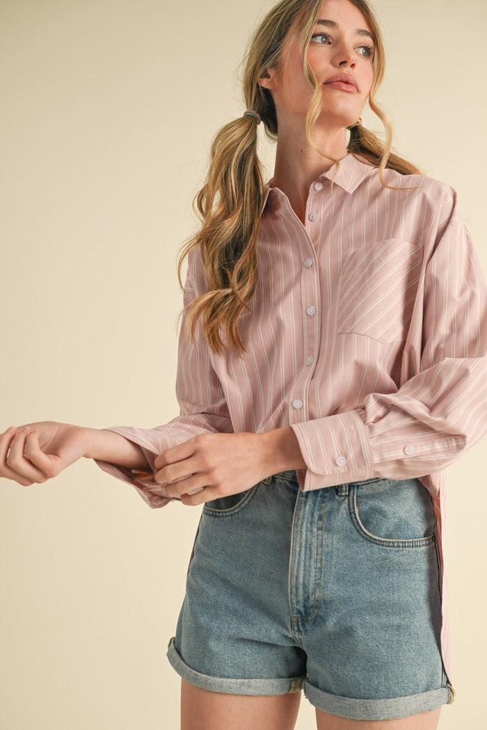 woman wearing a light pink striped long sleeve button-up shirt with a chest pocket and high-waisted denim shorts