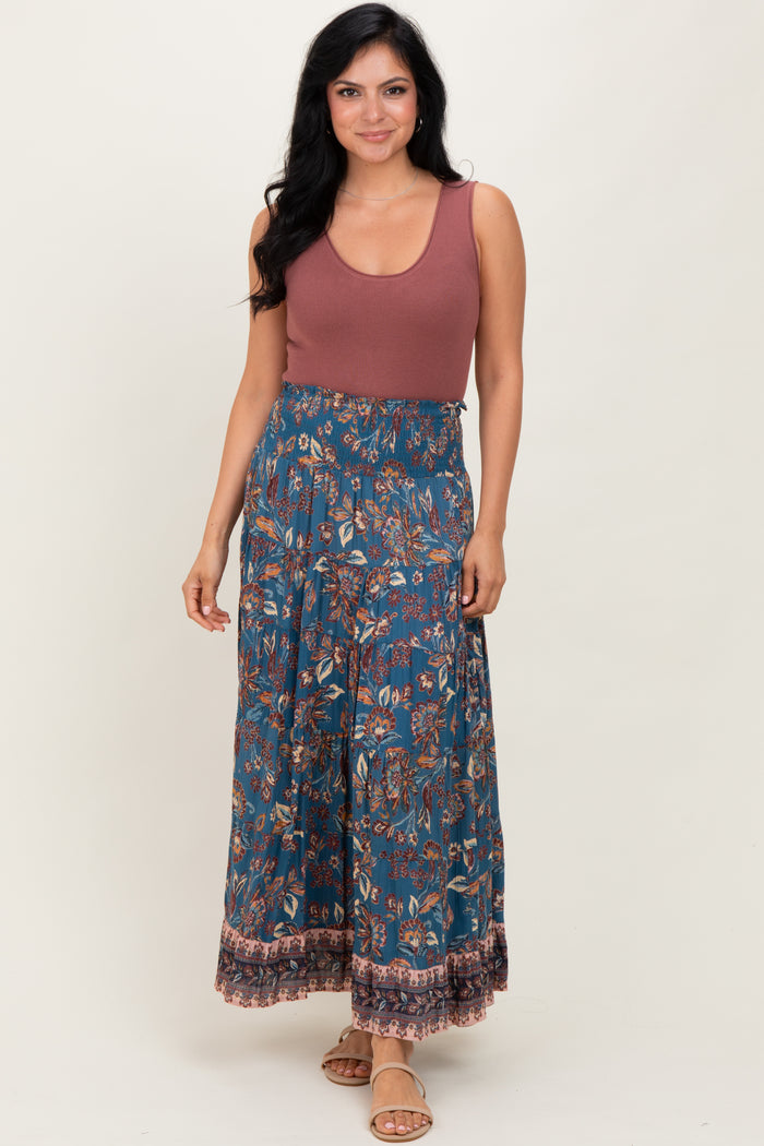 woman wearing a rust sleeveless top with a blue floral maxi skirt and sandals