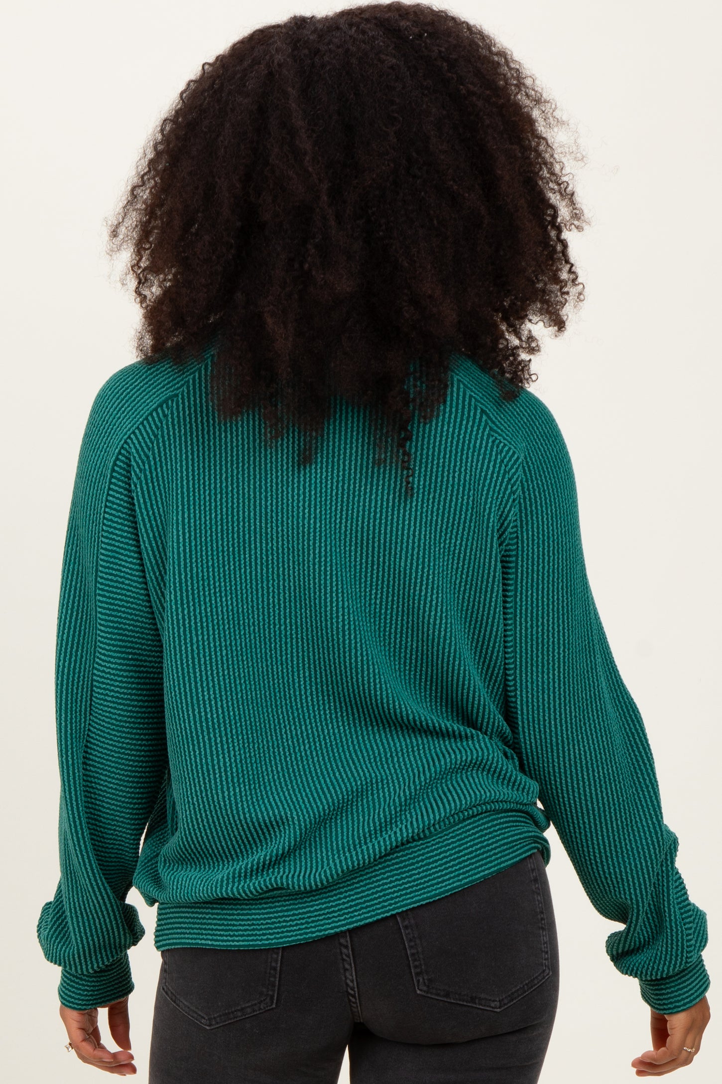 woman wearing a teal ribbed long sleeve sweater, viewed from the back, paired with black jeans