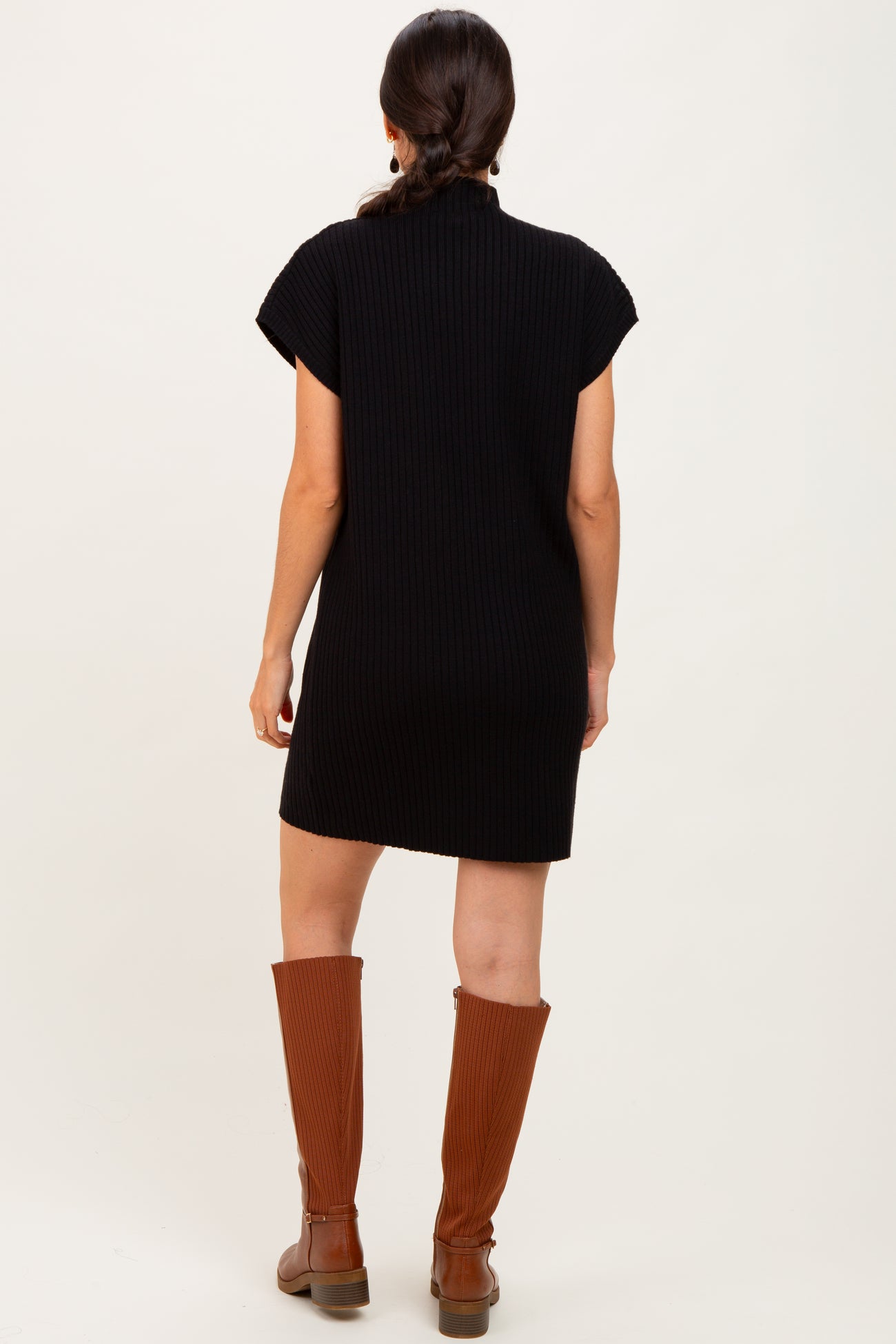 woman wearing a black ribbed short-sleeve dress and brown knee-high boots, seen from the back