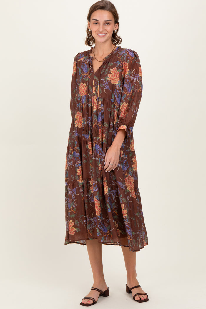 woman wearing a brown floral maxi dress with a tiered skirt and long sleeves, posing with a smile
