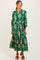 woman wearing a green floral maternity dress with long sleeves and a tiered skirt, smiling at the camera