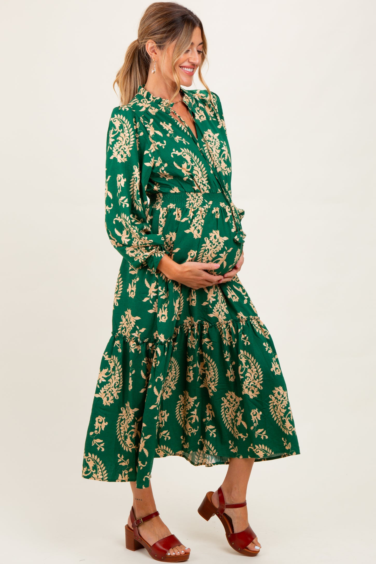 woman wearing a green floral maternity dress and holding her baby bump