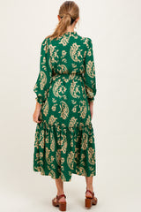 woman wearing a green floral patterned maternity dress with long sleeves and a tiered skirt
