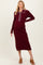 woman wearing a burgundy ribbed maternity dress with a collar and button detail, showcasing her baby bump