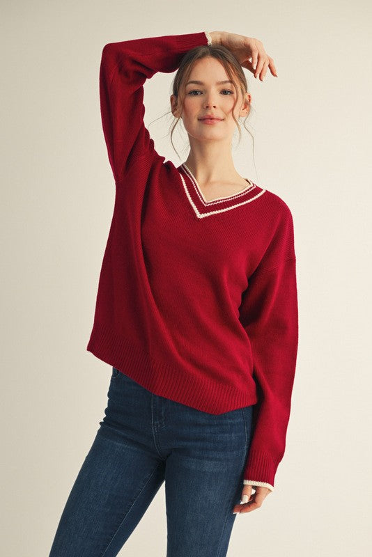 woman wearing a red v-neck sweater with white trim and blue jeans