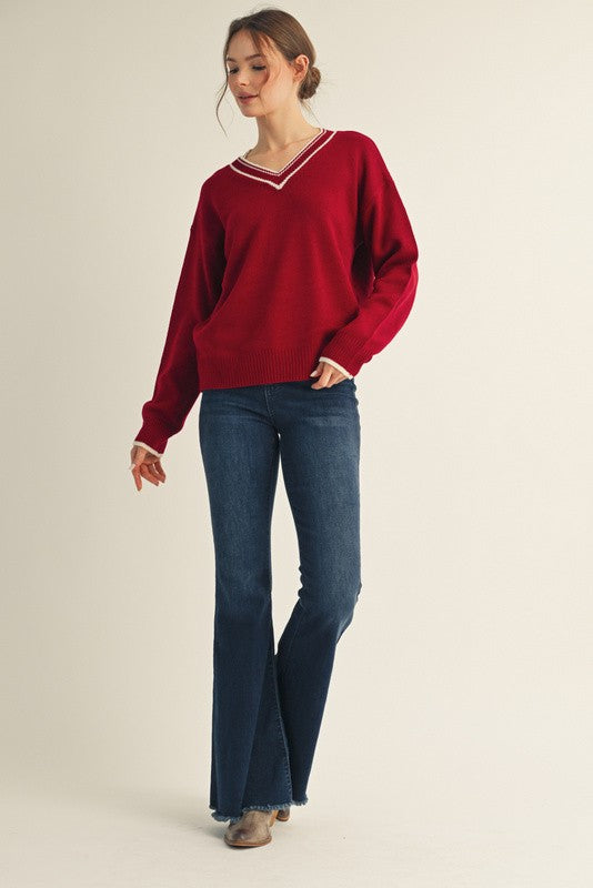 woman wearing a red v-neck sweater with white trim and flared blue jeans