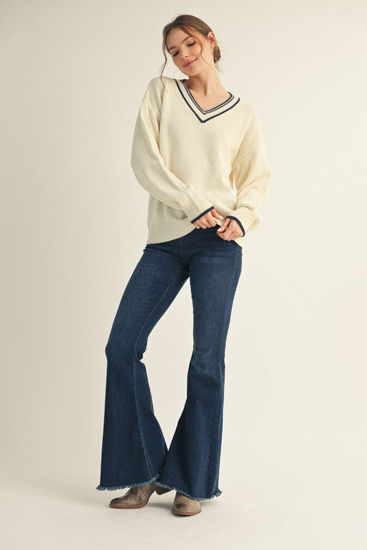 woman wearing a cream v-neck sweater with navy stripes and blue flared jeans