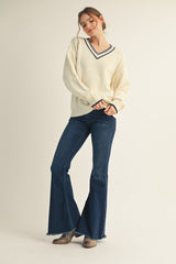 woman wearing a cream v-neck sweater with navy stripes and blue flared jeans