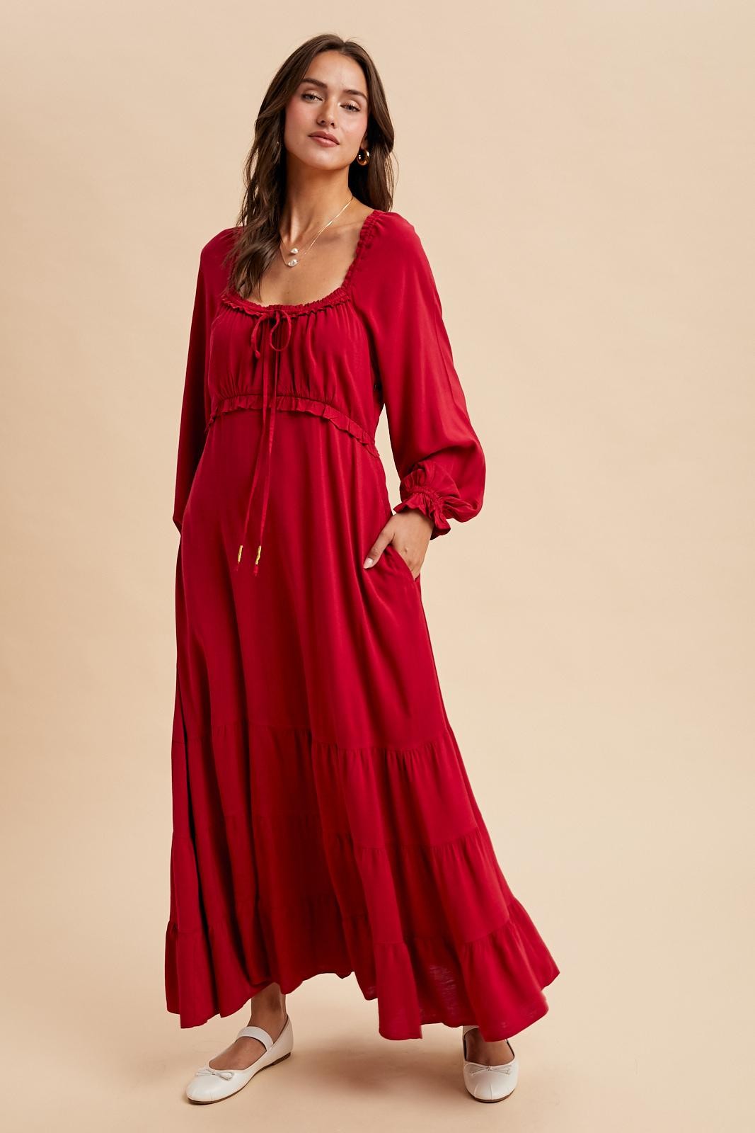 woman wearing a red maxi dress with a cinched waist, long sleeves, and ruffle details