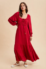 woman wearing a red long sleeve maxi dress with a cinched bodice and tiered skirt, styled with white flats
