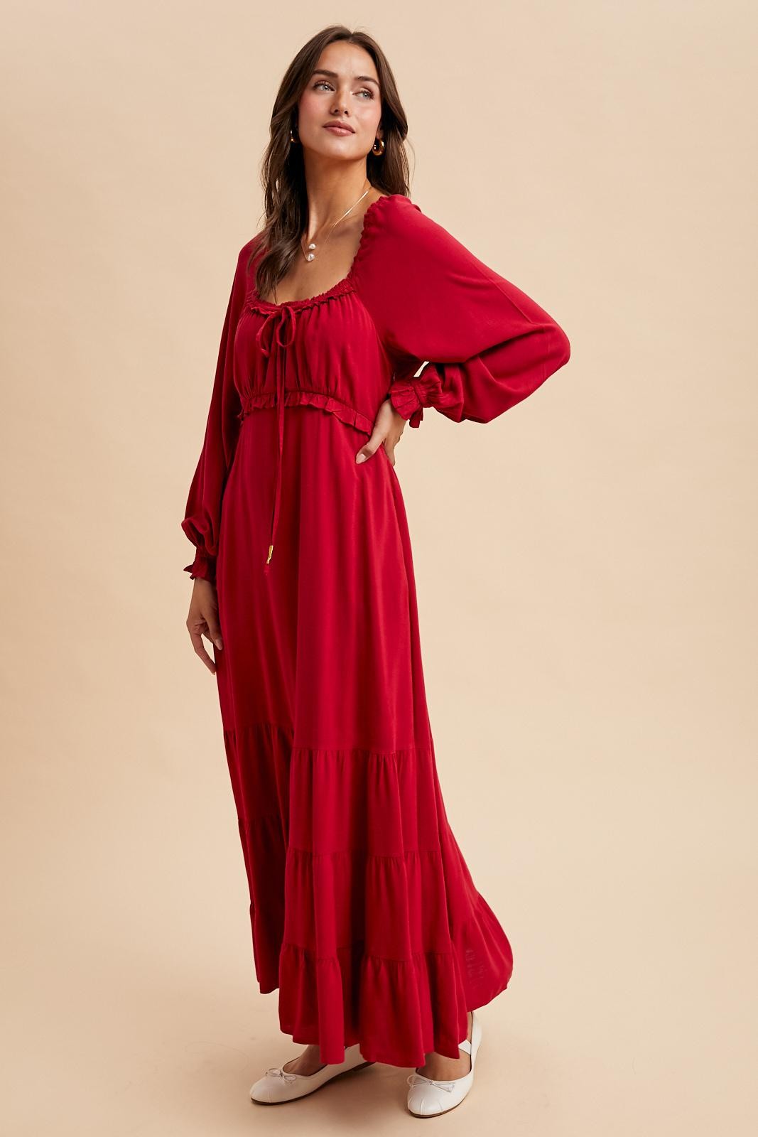 woman wearing a red maxi dress with a tie front, puff sleeves, and tiered skirt, styled with flat shoes