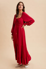 woman wearing a red maxi dress with a tie front, puff sleeves, and tiered skirt, styled with flat shoes