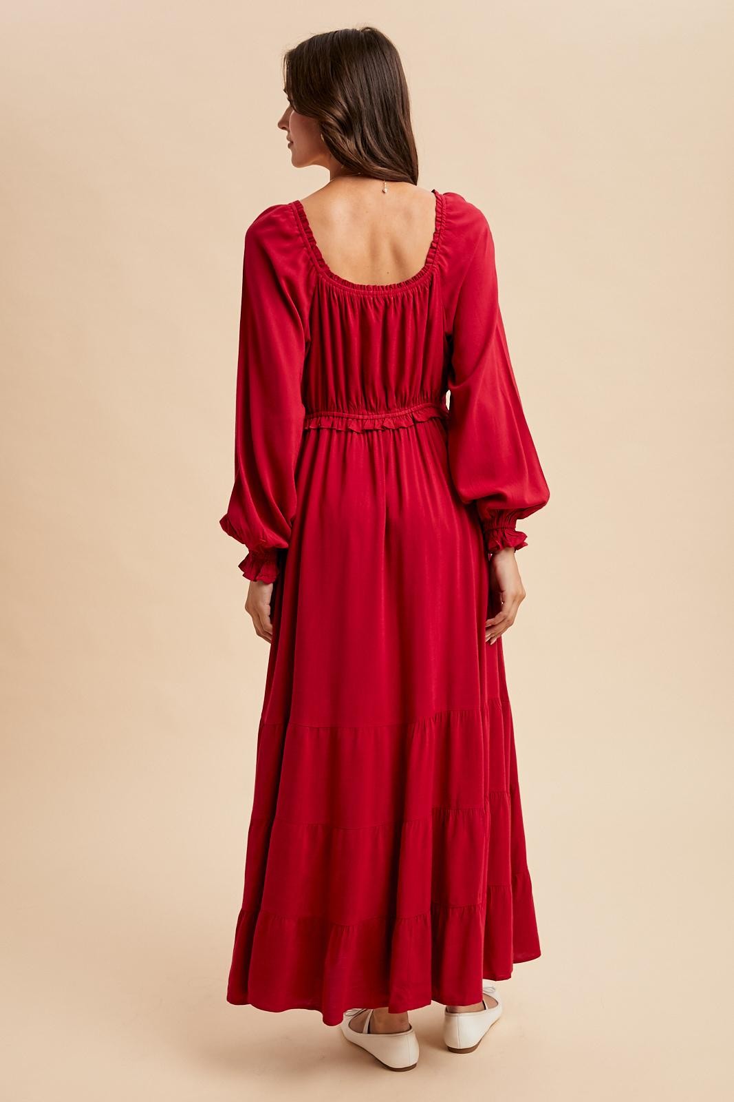 woman wearing a red long sleeve maxi dress with a tiered skirt and a fitted waist, seen from the back