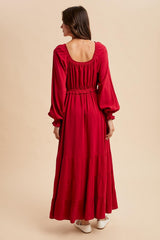woman wearing a red long sleeve maxi dress with a tiered skirt and a fitted waist, seen from the back