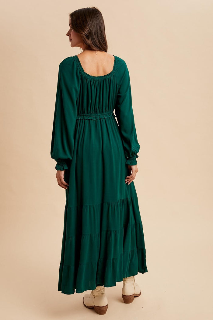 woman wearing a long green tiered maxi dress with long sleeves and a smocked waist, shown from the back